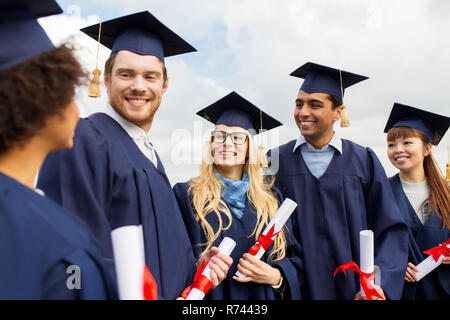 glückliche Schüler in Mörtel-Boards mit Diplomen Stockfoto