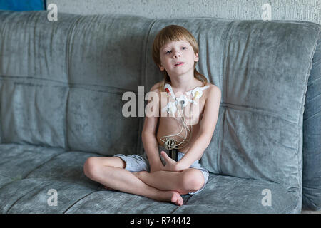 Kind auf dem Sofa sitzen. Herz Elektrokardiogramm oder Überwachung der Herzfunktion mit Holter. Stockfoto