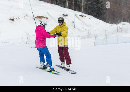 Junges Paar Snowboarder schieben Sie den Hang hinunter in einem Wintertag. Glückliches Paar Athleten. Stockfoto