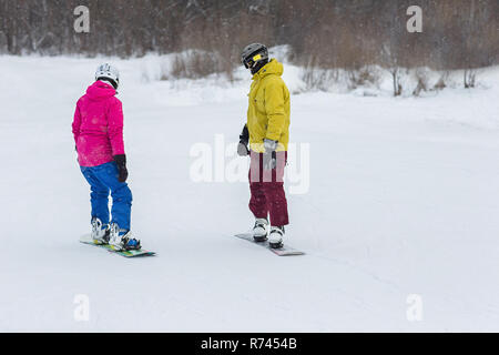 Junges Paar Snowboarder schieben Sie den Hang hinunter in einem Wintertag. Glückliches Paar Athleten. Stockfoto