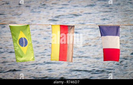 Verschiedene nationale Flaggen wave gegen einen Fluss im Hintergrund. Brasilien, Deutschland, Frankreich. Stockfoto