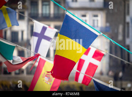 Flagge Rumänien Wellen inmitten von anderen nationalen Flaggen (Finnland, Dänemark, Schweden, Spanien), gegen eine alte Stadt Hintergrund. Stockfoto