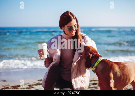 Stilvolle Mitte der erwachsenen Frau zusammengekauert am Strand ihren Hund streicheln, Odessa, Odeska Oblast, Ukraine Stockfoto