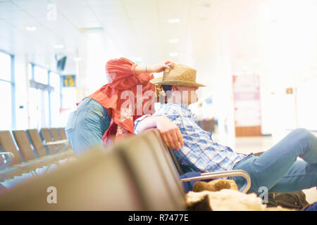Junger Mann am Flughafen sitzen, junge Frau ihren Hut auf den Kopf Stockfoto
