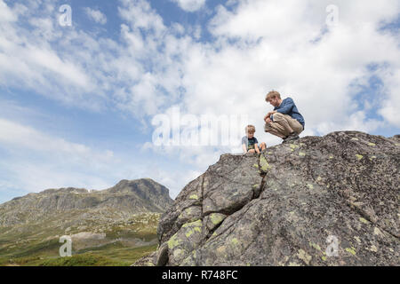 Junge und Vater kauernd auf Felsen, Low Angle View, Oppland, Nord-Trondelag, Norwegen Stockfoto