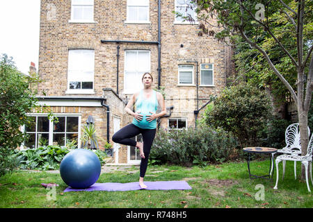 Schwangere Mitte der erwachsenen Frau yoga Baum im Garten Stockfoto