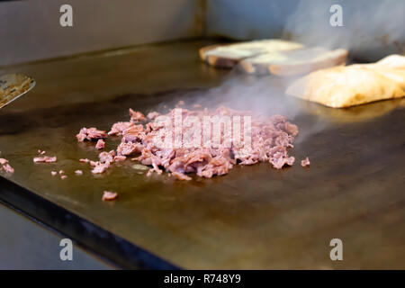 Die Herstellung eines Reuben Sandwich. Corned beef auf ein Restaurant oben flach Grill. Dampf steigt. Marmorierte Roggen Brot toasten im Hintergrund. Stockfoto