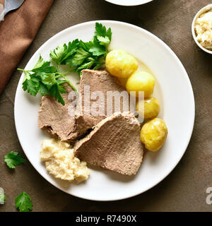 Nahaufnahme von gekochtem Rindfleisch mit Kartoffeln und Meerrettich (Tafelspitz) auf braunem Hintergrund. Ansicht von oben, flach Stockfoto