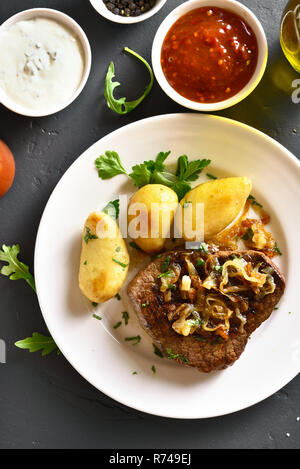 Lecker geschnitten Medium gebratenes Roastbeef mit Kartoffeln über schwarzen Stein. Ansicht von oben, flach Stockfoto