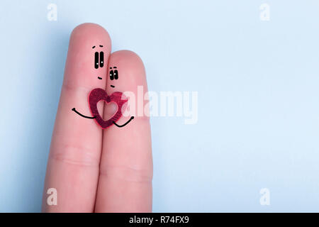 Finger mit einem dekorativen Herz und bemalten Gesichtern auf einem blauen Hintergrund, das Konzept von ein Paar in Liebe, Postkarte für den Valentinstag Stockfoto