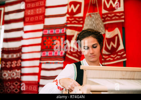 Vetka, Belarus - 23. Juni 2018: Die Frau in der ethnischen Traditionelle Völker nationalen weißrussischen Kostüm Kleid Weben am Webstuhl. Stockfoto