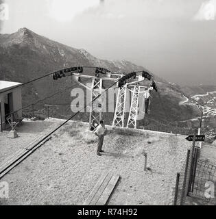 1960 s, historischen, einen Mann auf dem Sessellift auf den Gipfel des Monte Capanne auf der Insel Elba, Italien, mit der der Fahrer auf der Plattform, das 950 m über dem Meeresspiegel, der höchste Punkt auf der Insel. Mit dem Sessellift geht an Pozzatello, nahe dem Zentrum von Marciana. Stockfoto