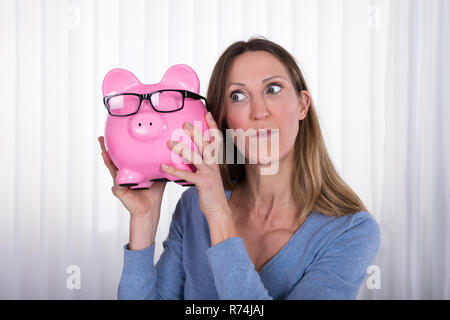 Reife Frau Holding Sparschwein mit Brillen Stockfoto