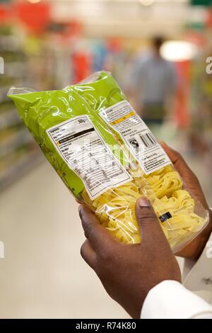 Eine schwarze Frau liest die Kennzeichnung von Lebensmitteln der ein Paket Nudeln in einem Supermarkt Stockfoto