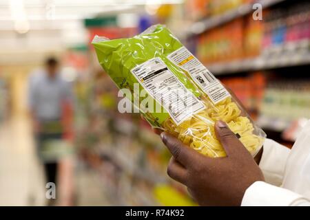 Eine schwarze Frau liest die Kennzeichnung von Lebensmitteln der ein Paket Nudeln in einem Supermarkt Stockfoto