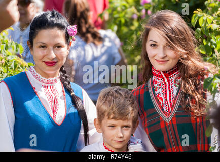 Frauen gekleidet in einem Bulgarischen traditionelle Folklore kostüm Kommissionierung Rosen in einen Garten, als Teil der Sommer regionale Ritual in Rose Valley, Bulgarien. Stockfoto