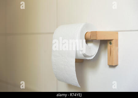 Eine weiße Rolle weiches Toilettenpapier ordentlich hängen an einem modernen Holz- Inhaber auf einem weiß gefliesten Badezimmer Wand. Stockfoto