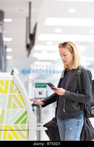 Casual kaukasische Frau mit Smart Phone Application und Check-in-Automaten am Flughafen erhalten der Bordkarte. Stockfoto