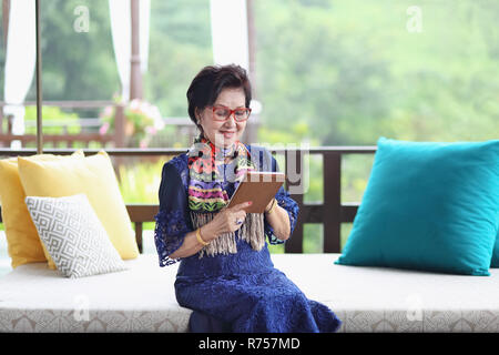 Asiatische ältere Frau auf dem Sofa sitzen und mit einem Tablet Stockfoto