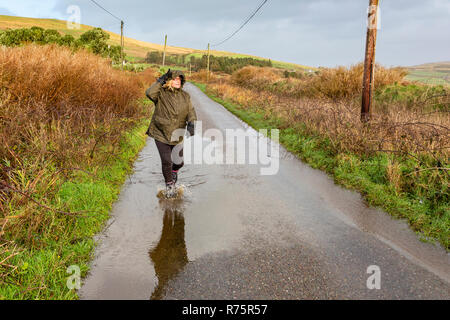 Frau Spritzen in Pfütze bei starkem Wind auf Grafschaft Lane im County Kerry Irland Stockfoto