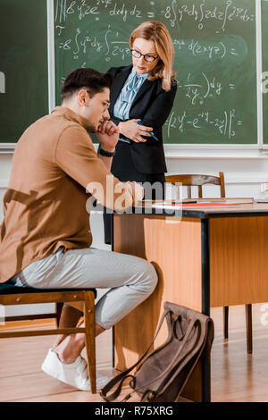 Frau Professor stand mit verschränkten Armen und nachdenkliche Schüler im Klassenzimmer Stockfoto