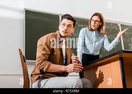 Unzufrieden Lehrerin in der Nähe von Tafel und sprechen mit Schülern im Klassenzimmer Stockfoto