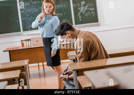 Selektiver Fokus der unzufriedenen Lehrerin auf männliche Kursteilnehmer betrug während der Untersuchung im Klassenzimmer Stockfoto