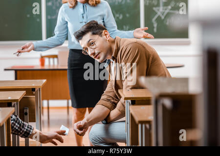 Selektiver Fokus der Unzufriedenen weiblichen Lehrer an der männlichen Kursteilnehmer die Krippe bei Untersuchung im Klassenzimmer auf der Suche Stockfoto