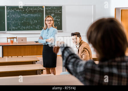 Selektiver Fokus der Lehrerin erklären, Unterrichtsmaterial, während männliche Kursteilnehmer auf Mitschüler Stockfoto