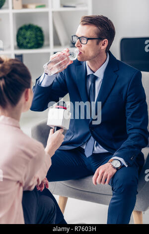 Gut aussehender Geschäftsmann Trinkwasser beim Geben Interview der Journalistin mit Mikrofon im Büro Stockfoto