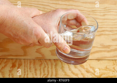 In einer Frau, die mit der Parkinson-Krankheit zitternde Hände so sehr, dass Sie ein Glas Wasser. Stark zitternden Hände einer Frau Stockfoto