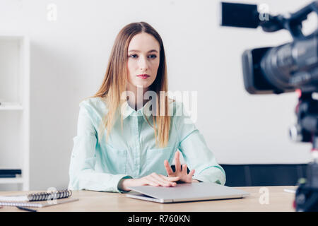 Attraktiven weiblichen video Blogger am Tisch mit Laptop und Aufzeichnung vlog im Büro zu sitzen Stockfoto