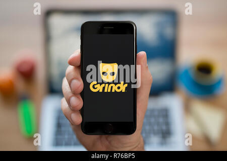 Ein Mann schaut auf seinem iPhone die zeigt die Grindr Logo (nur redaktionelle Nutzung). Stockfoto