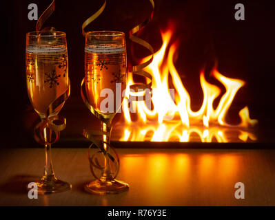 Zwei Gläser Champagner mit goldenen Bändern gegen die bokeh Hintergrund der hellen Flammen schaffen eine gemütliche Atmosphäre von Weihnachten oder Neujahr Stockfoto