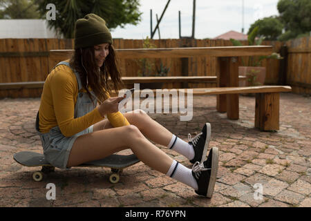 Weiblichen Skateboarder mit Handy beim Sitzen auf Skateboard Stockfoto