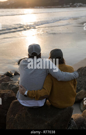 Paar sitzt auf Felsen in der Nähe von Strand Stockfoto