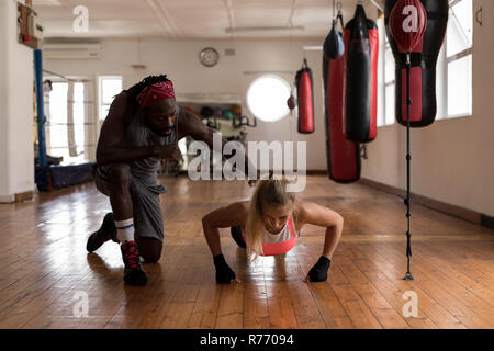 Trainer Unterstützung weiblicher Boxer dabei Push-ups im Fitness Studio. Stockfoto