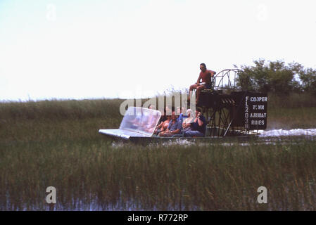 1970 s, Touristen, die auf einem Airboat in den Florida Everglades, ein Bereich der tropischen Feuchtgebiete in den USA. Die flachen Design der airboat ermöglicht eine einfache Navigation durch flachen Mooren und Sümpfen. Ökotourismus Airboating ist eine beliebte Attraktion. Coopertown Luftbootfahrten ist eine touristische Attraktion im Jahr 1945 gegründet. Stockfoto