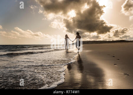 Romantischer Sonnenuntergang am Strand mit kaukasischen Schöne junge Paar waliing am Ufer - Flitterwochen und liebe Konzept für tausendjährigen Menschen - golden wa Stockfoto