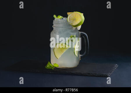 Ice Cold klassischen Kalk Limonade in einem vintage Glas Marmeladenglas. Der dunkle Hintergrund mit Kopie Raum für ein Menü. Stockfoto