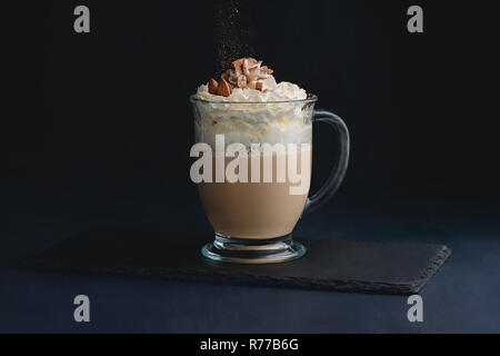 Kaffee und Milch latte Trinken mit Sahne, Nüsse und Kakaopulver. Süße heiße Getränke auf einem dunklen Hintergrund mit Kopie Raum für ein Menü Stockfoto