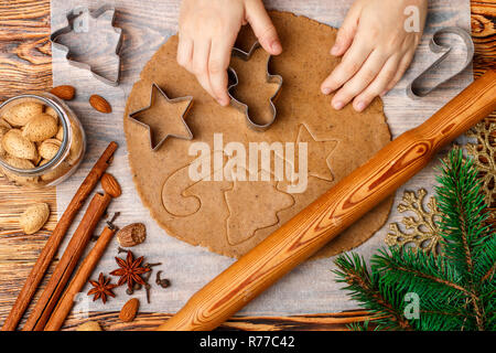 Baby's Händen macht traditionellen Lebkuchen. Gewürze auf dem Tisch - Anis, Kardamom, Zimt, Gewürznelken, Muskatnuss, Mandeln. Rohen Teig und Clippers in der Form Stockfoto