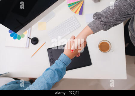 Designer diskutieren Angelegenheiten, während im Studio arbeiten, schüttelten ihre Hände. Ansicht von oben. Stockfoto