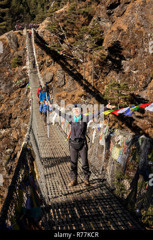 Nepal, Larja Dobhan, Senior weibliche Touristen mit ausgestreckten Armen feiern Kreuzung Obere Larja Hängebrücke über Dudh Khosi Fluss Stockfoto