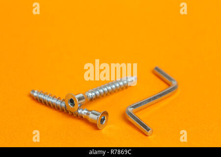 Metall Sechskantschlüssel und Möbel Schrauben Sechskant. Close-up auf orange Hintergrund Stockfoto