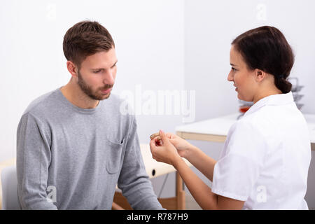 Junge männliche Patienten Betrachten Ärztin Holding Hörgerät In der Klinik Stockfoto