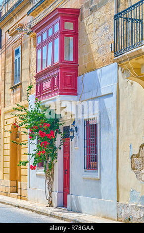 Das Wohnhaus in Mosta Stadt mit der roten Tür und maltesischen Stil Balkon, mit schönen Pflanze mit roten Blumen dekoriert Stockfoto