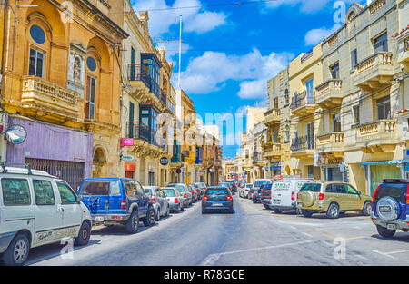 MOSTA, MALTA - 14. JUNI 2018: Der Verkehr in Il-Kbira Straße, mit alten Villen, Geschäften und Cafés gesäumt, die am 14. Juni in Mosta. Stockfoto