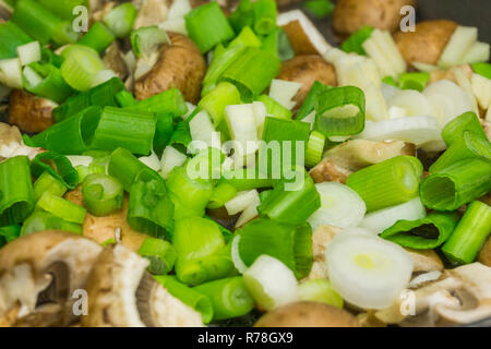 Nahaufnahme der gehackten grünen Frühlingszwiebeln und essbare Pilze in der Pfanne. Stockfoto