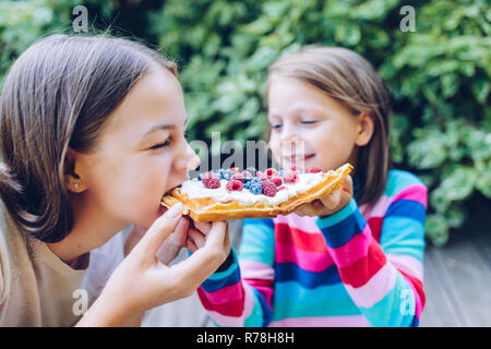 Waffeln - Mädchen essen eine Waffel mit Schlagsahne, Himbeeren und Heidelbeeren draußen im Garten zu lächeln und zu lachen Stockfoto